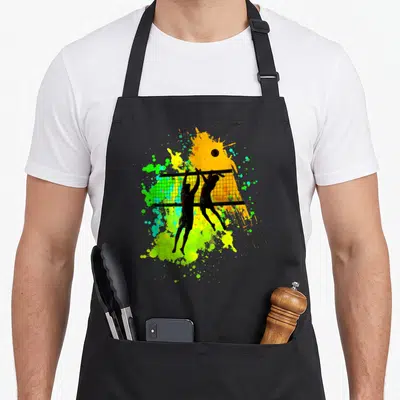 Tablier de cuisine noir avec deux silhouettes de joueurs de volley-ball sautant au-dessus du filet sur un fond d'éclaboussures colorées.