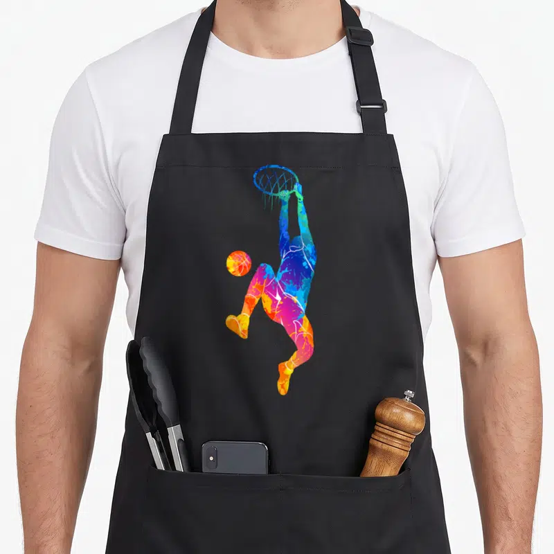 Tablier de cuisine noir avec silhouette colorée d'un joueur de basketball effectuant un dunk dynamique.