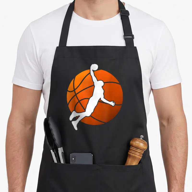 Tablier de cuisine noir avec silhouette blanche de joueur de basket en saut sur fond de ballon orange stylisé.