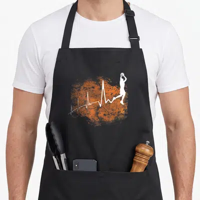 Tablier de cuisine noir avec silhouette blanche d'un joueur de basket-ball en saut et ligne de battement de cœur sur fond orange texturé.