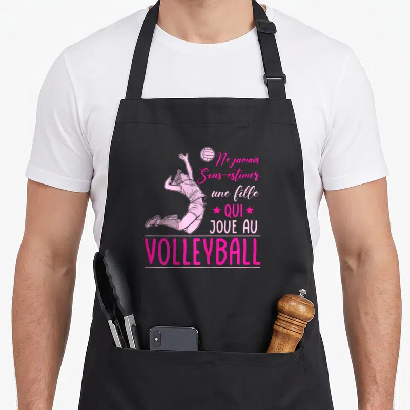 Tablier de cuisine noir avec illustration rose d'une femme effectuant un saut de volley et texte motivationnel imprimé.