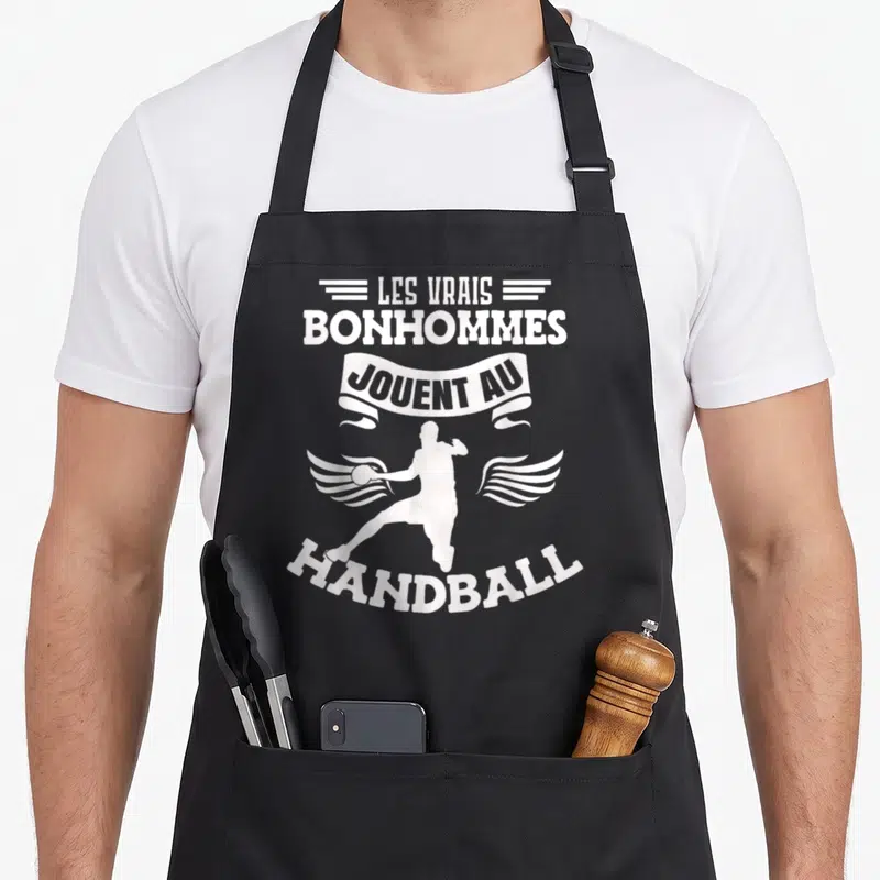 Tablier de cuisine noir avec silhouette blanche d'un handballeur ailé et texte Les vrais bonhommes jouent au handball.