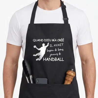 Tablier de cuisine noir avec silhouette blanche de handballeur et texte quand dieu m'a créé il avait besoin de bons joueurs de handball
