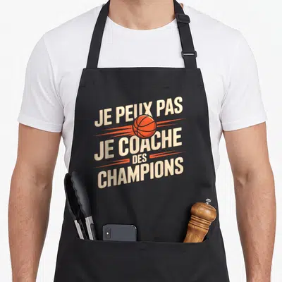Tablier de cuisine noir avec l'inscription Je peux pas je coache des champions et un ballon de basket orange au centre du design typographique.