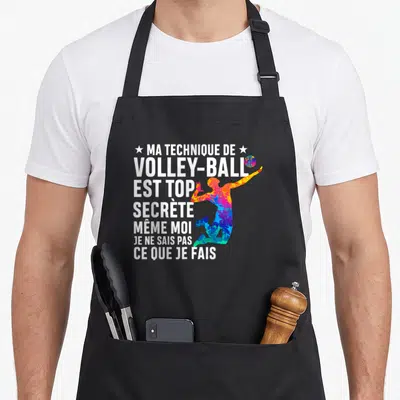 Tablier de cuisine noir avec silhouette multicolore de joueur de volley et texte blanc humoristique sur la technique secrète.