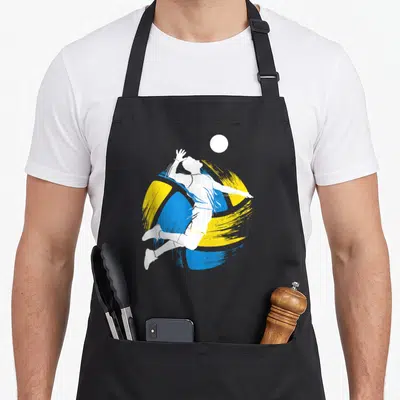 Tablier de cuisine noir avec silhouette blanche sautant vers un ballon sur fond de traits bleus et jaunes.