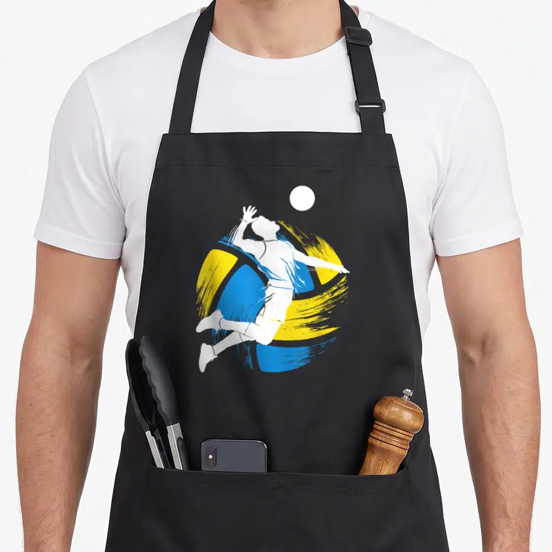 Tablier de cuisine noir avec silhouette blanche sautant vers un ballon sur fond de traits bleus et jaunes.