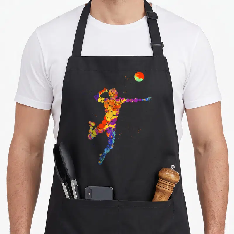 Tablier de cuisine noir avec une illustration d'un joueur de volley-ball formé par des éclats de couleurs vives et abstraites.