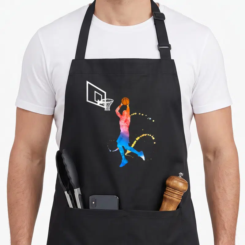 Tablier de cuisine noir avec silhouette aquarelle d'un joueur de basket effectuant un panier sous le cerceau.