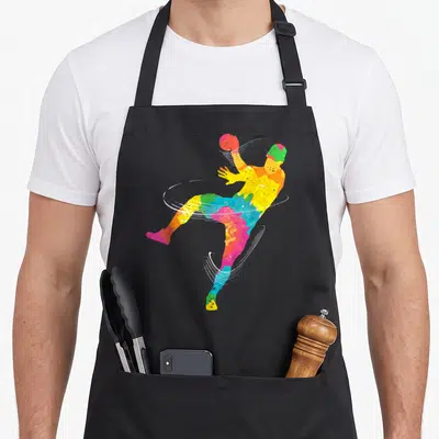 Tablier de cuisine noir avec illustration colorée d'un handballeur en saut et lignes blanches dynamiques.