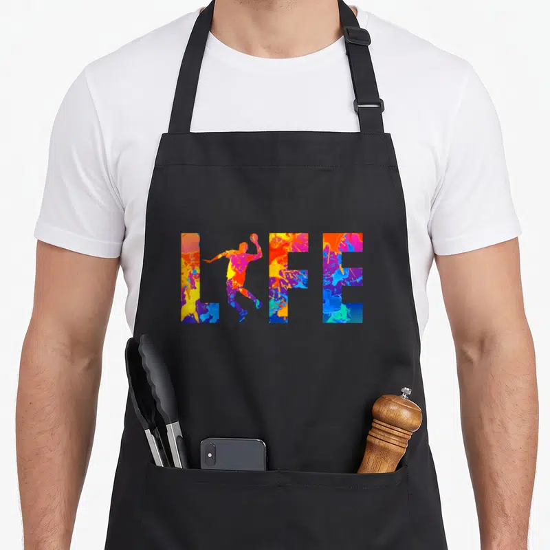 Tablier de cuisine noir avec le mot LIFE en lettres multicolores et une silhouette de joueur de handball au centre.