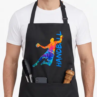 Tablier de cuisine noir avec une illustration multicolore d'un handballeur en action et le texte HANDBALL vertical à côté.