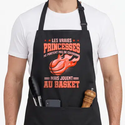 Tablier de cuisine noir avec un ballon de basket enflammé et le texte Les vraies princesses ne portent pas de couronne mais jouent au basket.