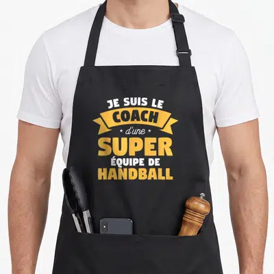 Tablier de cuisine noir avec l'inscription Je suis le coach d'une super équipe de handball en blanc et jaune doré.