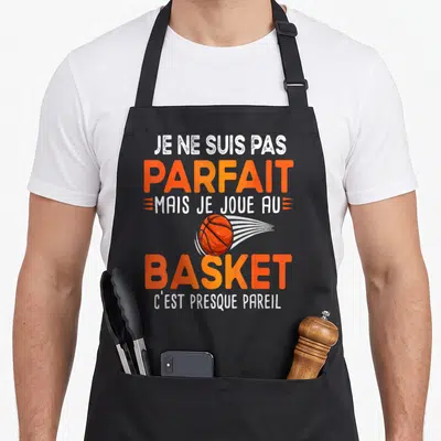 Tablier de cuisine noir avec une balle de basket orange et le texte Je ne suis pas parfait mais je joue au basket en lettres blanches et oranges.
