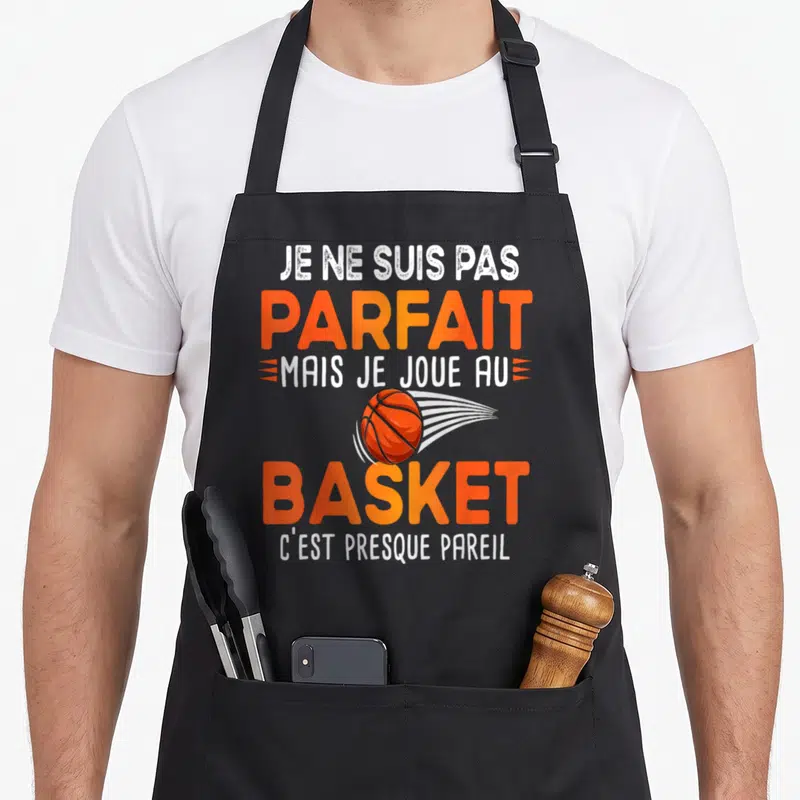 Tablier de cuisine noir avec une balle de basket orange et le texte Je ne suis pas parfait mais je joue au basket en lettres blanches et oranges.