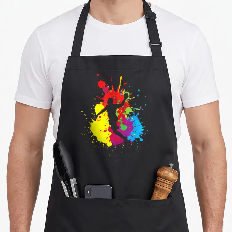 Tablier de cuisine noir avec silhouette de joueur de handball entourée d'éclaboussures de peinture jaune, rouge, bleu et vert vif.