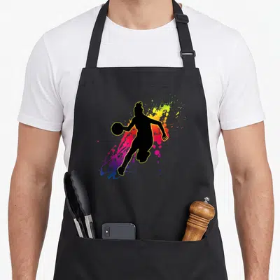 Tablier de cuisine noir avec silhouette joueuse de basket aux éclaboussures colorées.