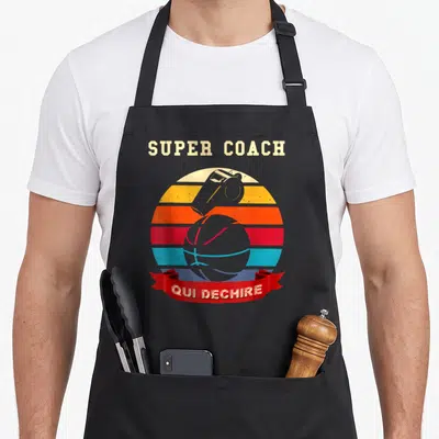Tablier de cuisine noir avec illustration retro d'un ballon de basket et d'un sifflet sous le texte Super Coach Qui Déchire.