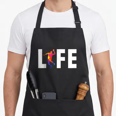 Tablier de cuisine noir avec une illustration d'un joueur de handball formant le mot LIFE en lettres blanches et couleurs vives.