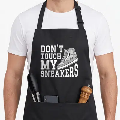 Tablier de cuisine noir avec illustration de sneaker blanche et texte Don't Touch My Sneakers en typographie sport.