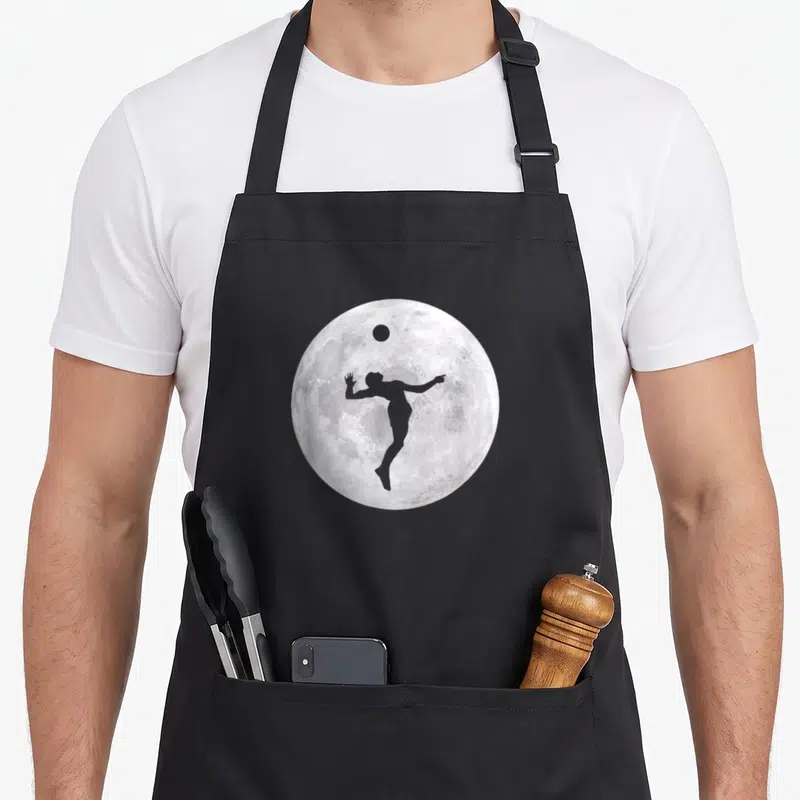 Tablier de cuisine noir avec silhouette de joueur de volley devant une pleine lune détaillée.