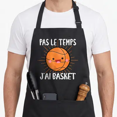 Tablier de cuisine noir avec un ballon de basket-ball souriant et une inscription blanche humoristique.