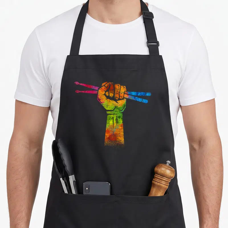 Tablier de cuisine noir avec illustration d'une main multicolore serrant deux paires de baguettes de batterie roses et bleues.