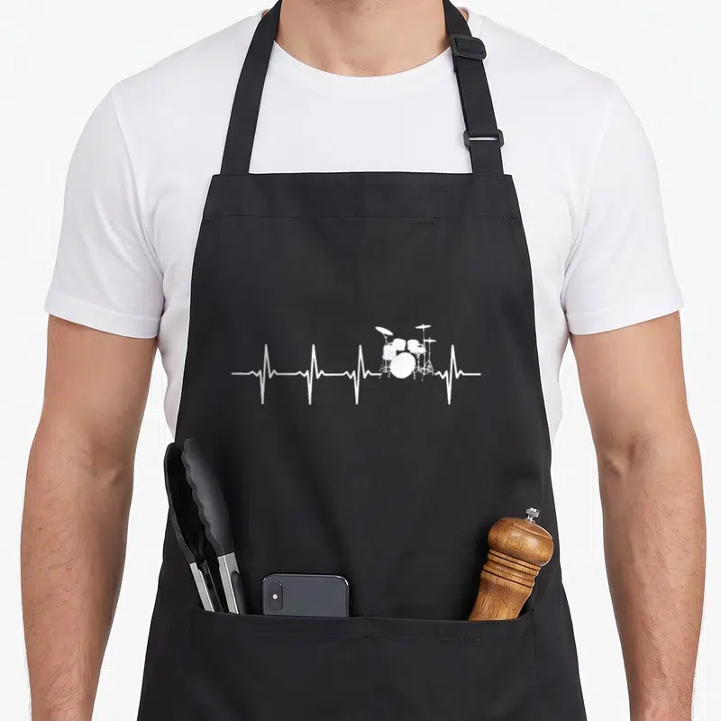Tablier de cuisine noir avec un motif blanc représentant une ligne de battement de cœur transformée en kit de batterie.