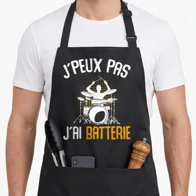 Tablier de cuisine noir avec inscription J'peux pas j'ai batterie et silhouette de batteur blanc sur fond orange.
