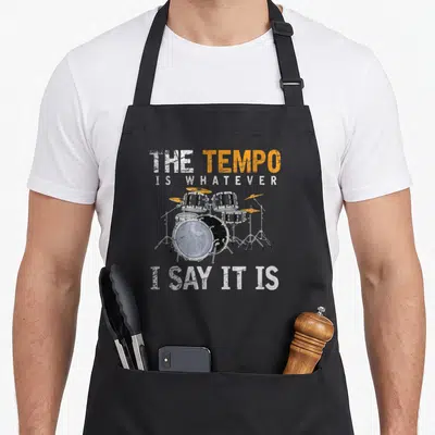 Tablier de cuisine noir avec illustration de batterie et texte anglais The tempo is whatever I say it is en orange et blanc.
