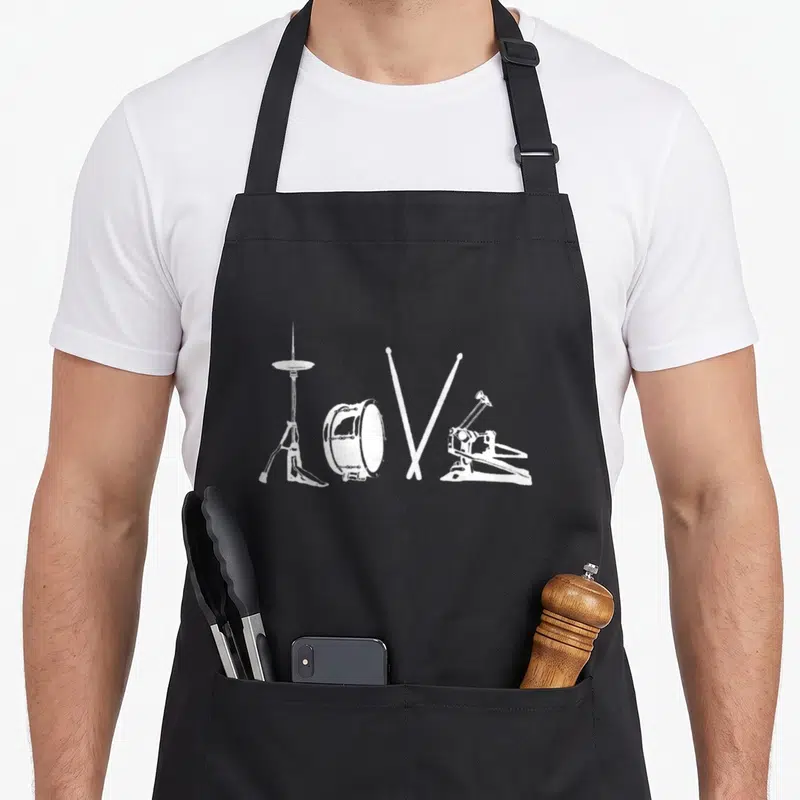 Tablier de cuisine noir avec illustration blanche représentant un cymbalier, un tambour, deux baguettes croisées et une pédale de basse forming le mot Love.