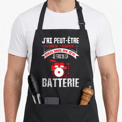 Tablier de cuisine noir avec une illustration de batterie rouge et un slogan humoristique en blanc et rouge sur fond uni.