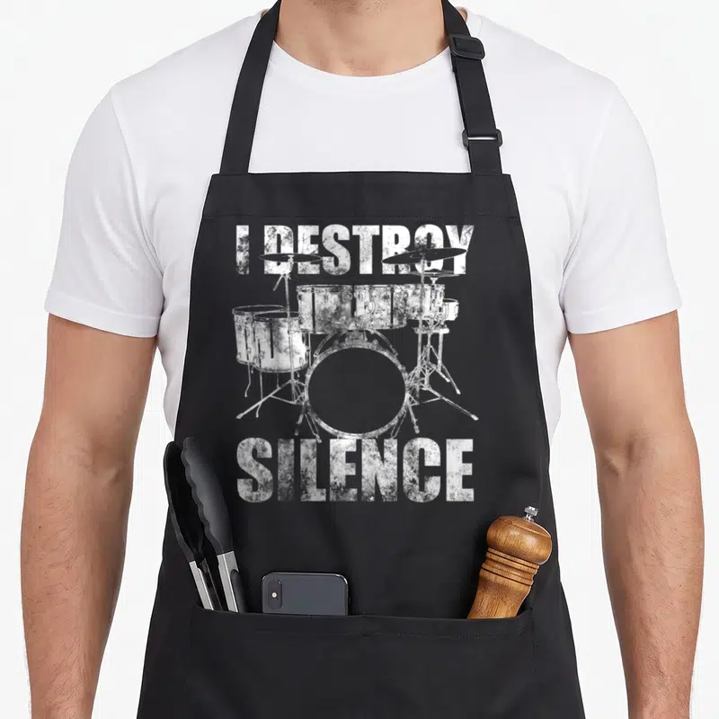 Tablier de cuisine noir avec illustration blanche de batterie et texte I DESTROY SILENCE en typographie usée.