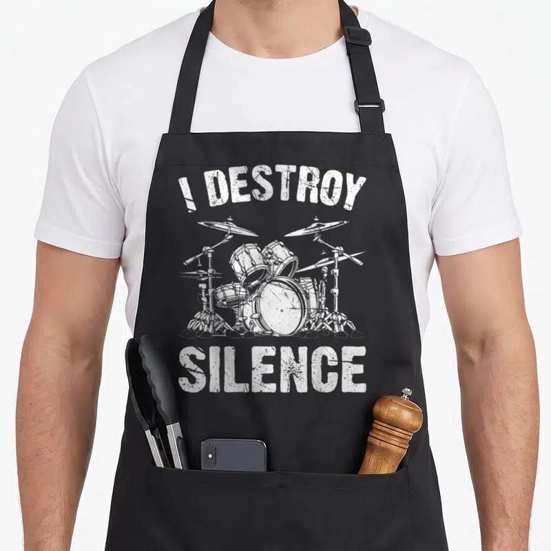 Tablier de cuisine noir avec illustration blanche d'un kit de batterie vintage et le texte I Destroy Silence en typographie usée.