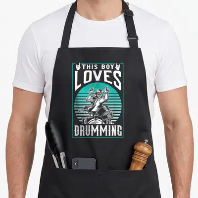 Tablier de cuisine noir avec illustration d'un batteur tenant des baguettes sous le texte This Boy Loves Drumming