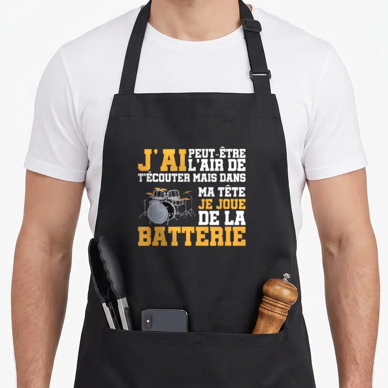 Tablier de cuisine noir avec texte jaune et blanc sur la batterie et un dessin de kit percussions au centre.