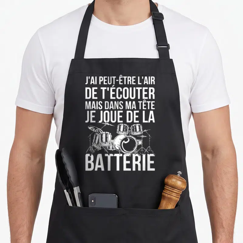 Tablier de cuisine noir avec l'inscription blanche J'ai peut-être l'air de t'écouter mais dans ma tête je joue de la batterie au-dessus d'un dessin de kit.