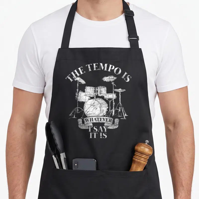 Tablier de cuisine noir avec illustration blanche d'un set de batterie et le texte The Tempo Is Whatever I Say It Is