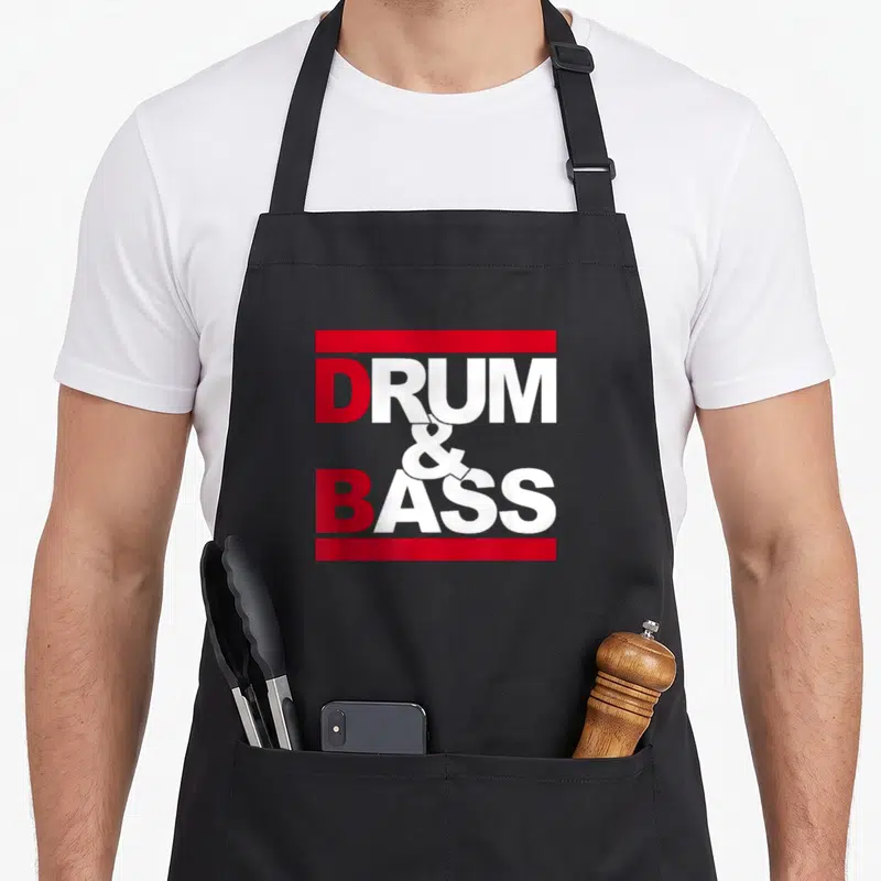 Tablier de cuisine noir avec l'inscription Drum & Bass en lettres rouges et blanches encadrées par des bandes horizontales.