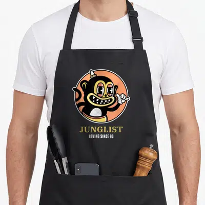 Tablier de cuisine noir avec illustration circulaire d'un singe noir et orange et le texte Junglist Raving Since 95 imprimé en dessous.