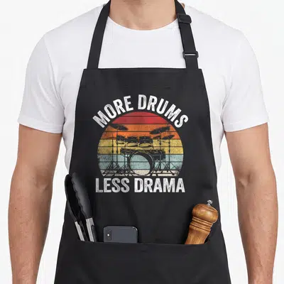 Tablier de cuisine noir avec illustration vintage d'un set de batterie et texte blanc More Drums Less Drama.