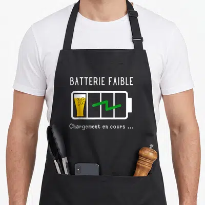 Tablier de cuisine noir avec une illustration de batterie faible contenant un verre de bière et du texte humoristique.