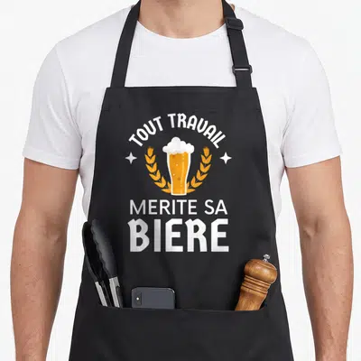 Tablier de cuisine noir avec un verre de bière doré, des épis de wheat et le texte tout travail mérite sa bière en blanc.