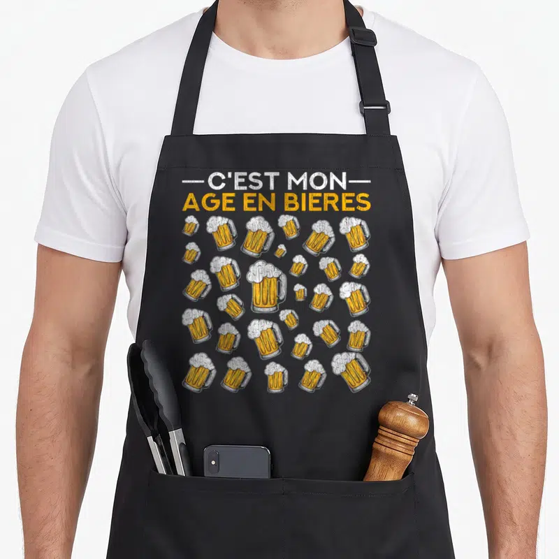 Tablier de cuisine noir orné de multiples verres de bière et du texte C'est mon âge en bières en lettres orange et blanches.