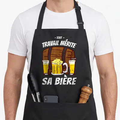 Tablier de cuisine noir avec un tonneau en bois, trois verres de bière et le texte tout travail mérite sa bière imprimé en blanc.