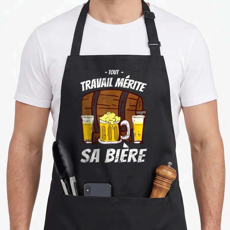 Tablier de cuisine noir avec un tonneau en bois, trois verres de bière et le texte tout travail mérite sa bière imprimé en blanc.