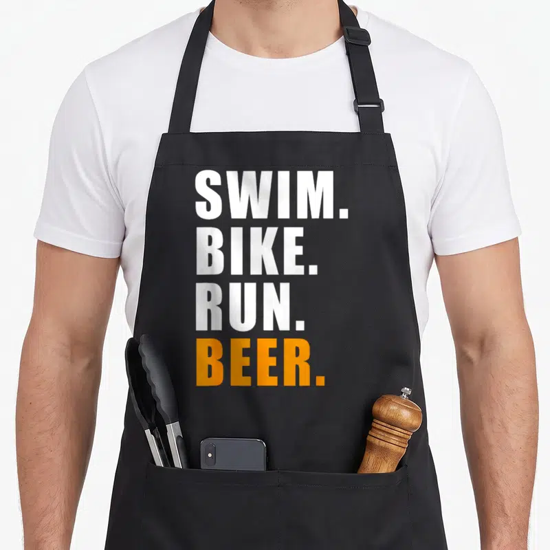 Tablier de cuisine noir avec l'inscription Swim Bike Run Beer en lettres blanches et oranges sur fond uni.