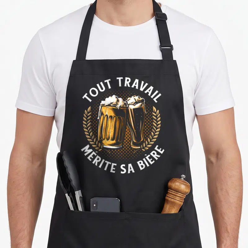 Tablier de cuisine noir avec deux verres de bière en toast et texte Tout travail mérite sa bière entouré de couronnes de malt.