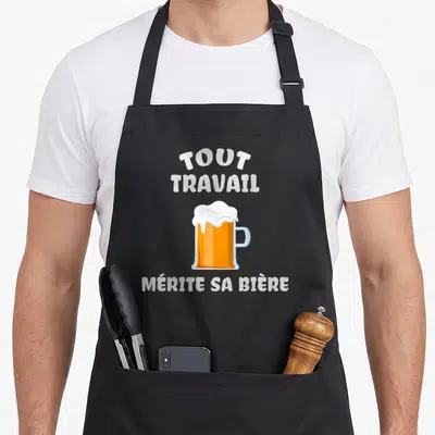 Tablier de cuisine noir avec inscription tout travail mérite sa bière et illustration de mug de bière à la mousse blanche.